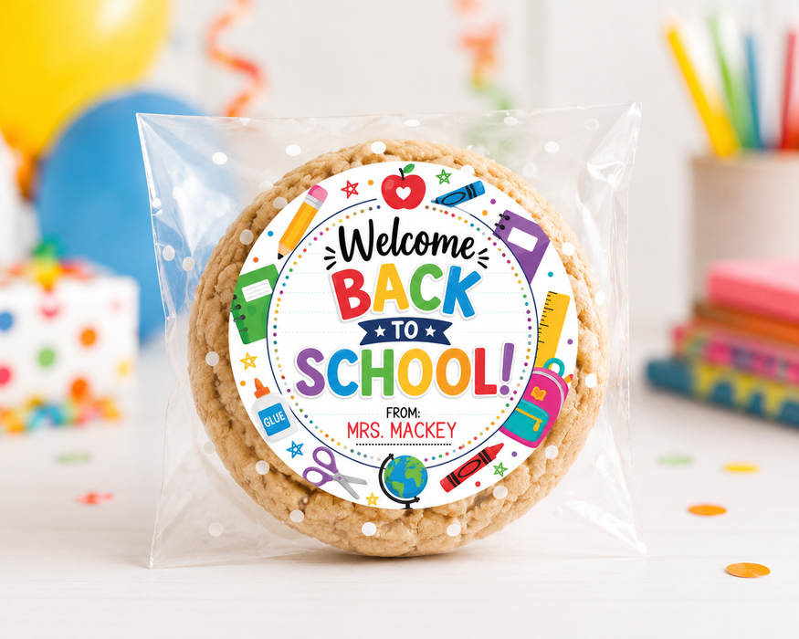 A round sugar cookie sealed in a clear plastic bag with a colorful circular 'Welcome Back to School!' label. The label includes school-themed illustrations and the text 'FROM: MRS.