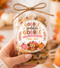 A hand holds a clear cellophane bag of chocolate chip cookies tied with a twine bow. The front has a round printed label reading 'Gobble gobble Happy Thanksgiving From, Libby' with autumn illustrations.