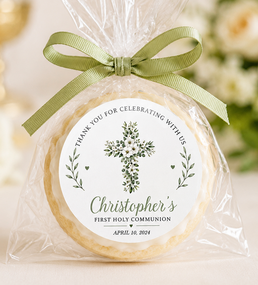 A round cookie or biscuit wrapped in clear cellophane and tied with an olive green ribbon, featuring a personalized round label that reads 'Christopher's First Holy Communion' with a floral cross design.
