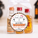 A Halloween-themed gift set in a clear cellophane bag tied with a white ribbon, containing three miniature whiskey bottles with orange and red caps. A round sticker on the front reads 'you've been BOOZED! Happy Halloween from The Weebles' with cartoon ghosts.