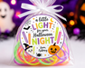 A clear cellophane bag filled with bright neon rubber bands, tied with a white ribbon and labeled 'a little LIGHT for your Halloween NIGHT from Aubrey' with Halloween illustrations, set against a festive blurred purple background.