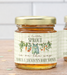 Two glass jars of honey with gold lids and personalized labels, displayed on a wooden surface with a soft-focus background.