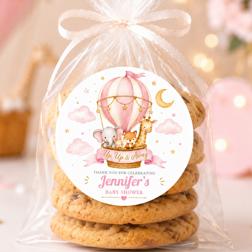 A clear cellophane bag tied with a white ribbon, containing a stack of cookies, with a round printed label on the front. The label features a pink hot air balloon, giraffe, moon, and the text 'You are so dear Jennifer's baby shower'.