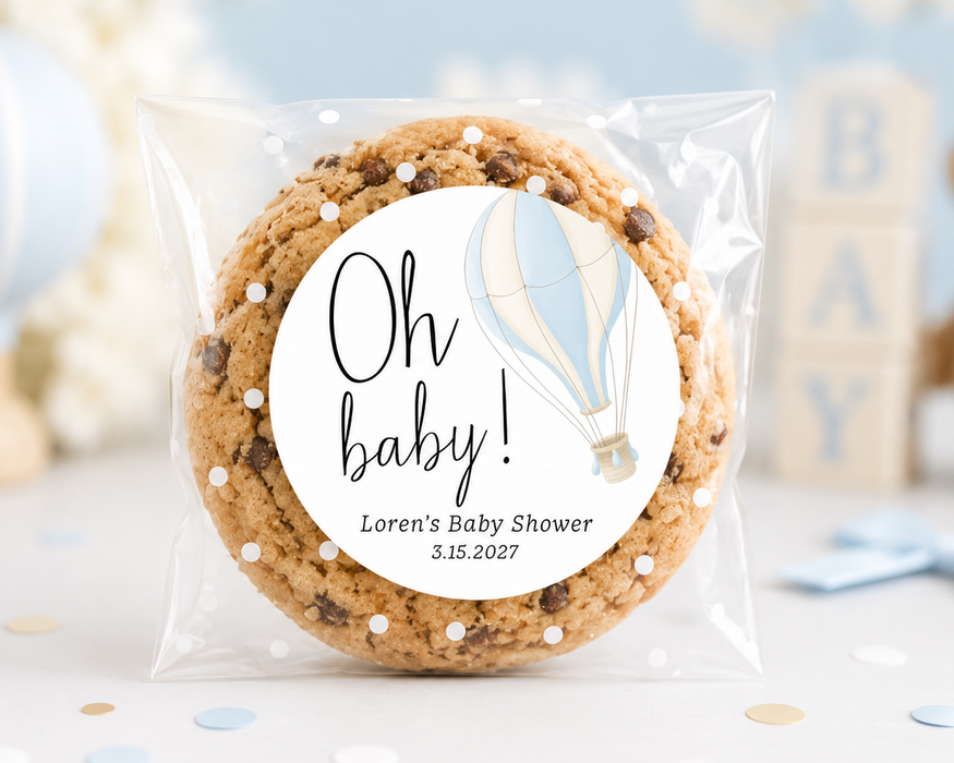 A round chocolate chip cookie in a clear plastic bag with a round white label that reads 'Oh baby! Loren's Baby Shower 3.15.