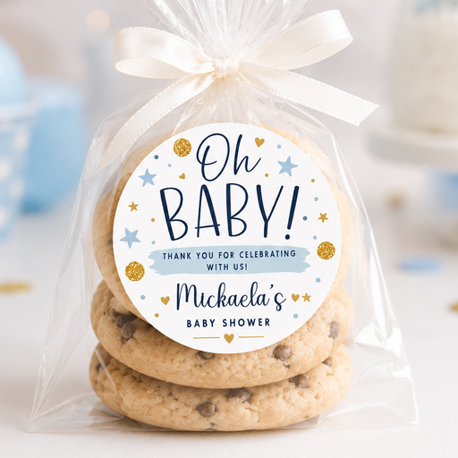 A clear cellophane bag tied with a white ribbon, containing three stacked chocolate chip cookies, with a round printed label that reads 'Oh BABY! Thank you for celebrating with us! Michaela's Baby Shower.' The scene is softly lit and decorated with pastel blue balloons and party confetti in the background.