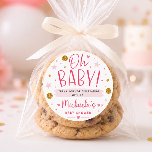 A clear cellophane bag tied with a cream ribbon, containing chocolate chip cookies and a round printed label that reads 'Oh BABY! Michaela's Baby Shower.' The scene is styled with pink and white balloons, confetti, and soft party decorations in the background.