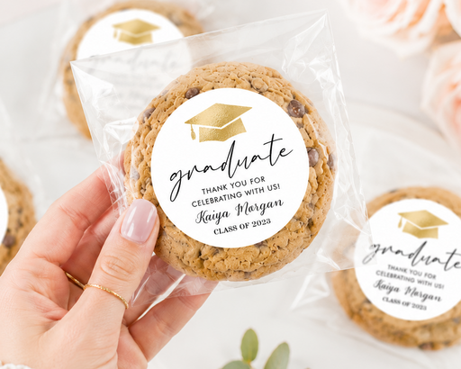 Cookies with 'graduate' labels held by a hand, surrounded by flowers and greenery.