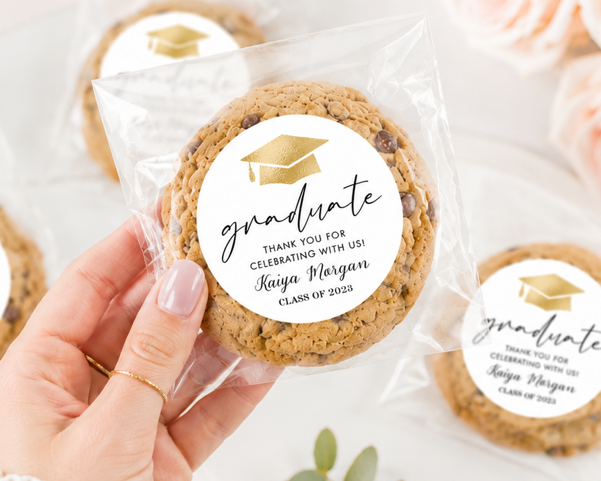 Cookies with 'graduate' labels held by a hand, surrounded by flowers and greenery.