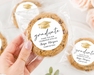 Cookies with 'graduate' labels held by a hand, surrounded by flowers and greenery.