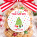 A clear cellophane gift bag filled with Christmas cookies and tied with a red-and-white striped ribbon, featuring a round 'Merry Christmas From The Millers' label. The bag is photographed on a marble surface with festive holiday decorations in the background.