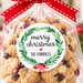 A bag of holiday cookies tied with a red ribbon and a round 'merry christmas' label, set on a marble surface with a blurred Christmas tree and ornaments in the background.