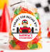 A clear cellophane bag filled with colorful gummy candies and tied with a clear twist tie, featuring a round racing-themed label that reads 'THANKS FOR RACING BY! ANDREW'S 5TH BIRTHDAY' with a cartoon driver in a red race car. The bag is photographed on a white party surface with blurred balloons, checkered backdrop elements, and toy cars in the background.