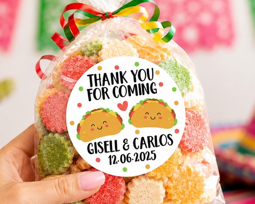 A hand holds a clear plastic bag filled with colorful gummy candies tied with a red, green, and yellow striped ribbon. The bag has a round white label that reads 'THANK YOU FOR COMING' with taco illustrations and the names 'Gisell & Carlos' plus a date.