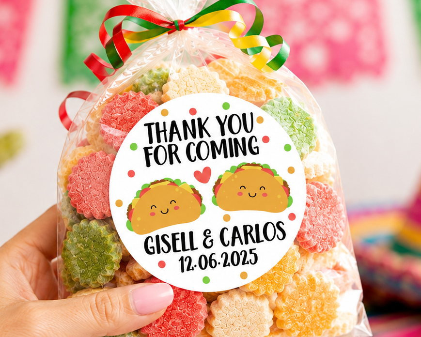 A hand holds a clear plastic bag filled with colorful gummy candies tied with a red, green, and yellow striped ribbon. The bag has a round white label that reads 'THANK YOU FOR COMING' with taco illustrations and the names 'Gisell & Carlos' plus a date.