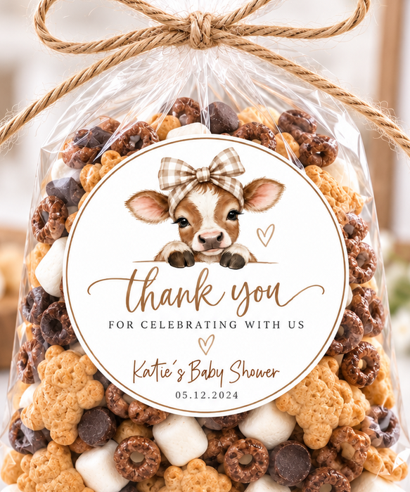 A clear cellophane gift bag filled with assorted baby shower mix, tied with a twine bow and labeled with a custom cow graphic and the text 'thank you for celebrating with us Katie & Baby Shower 05.12.